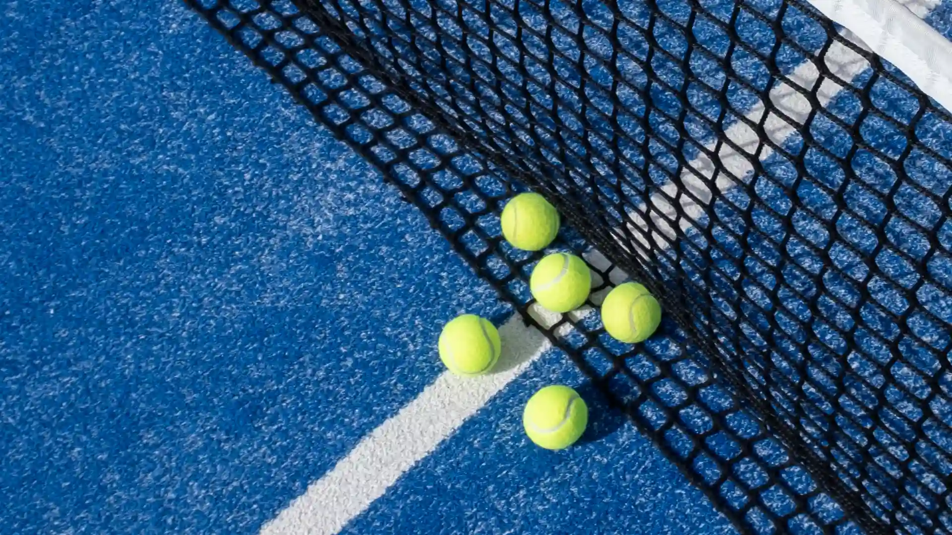 Padel balls placed beside the net on a blue outdoor padel court