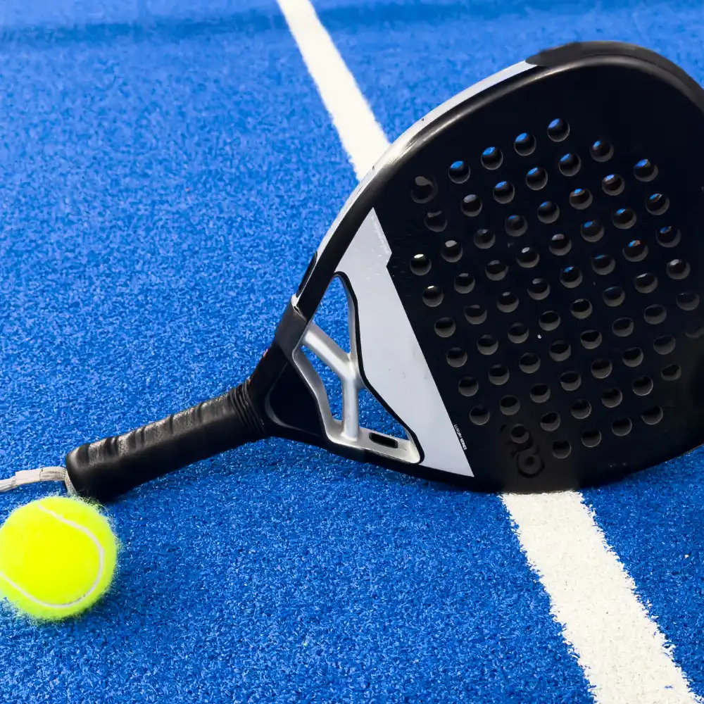 Black padel racket and ball positioned on a blue padel court surface