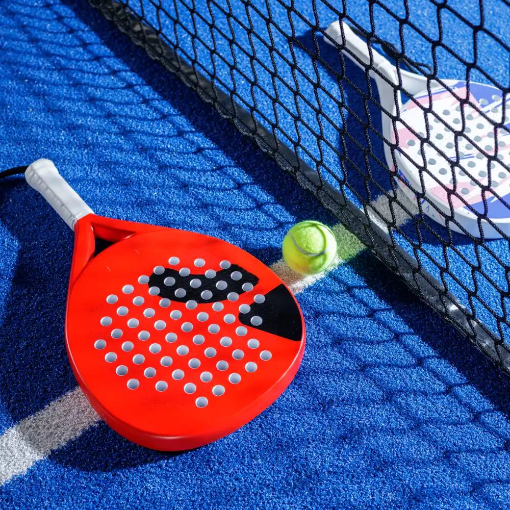 Red padel racket and ball placed beside the net on a blue padel court