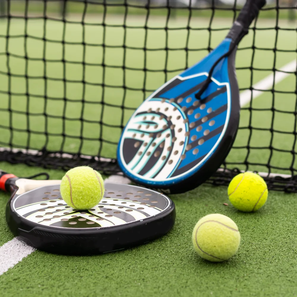 Two padel rackets and tennis balls placed beside the net on an outdoor court