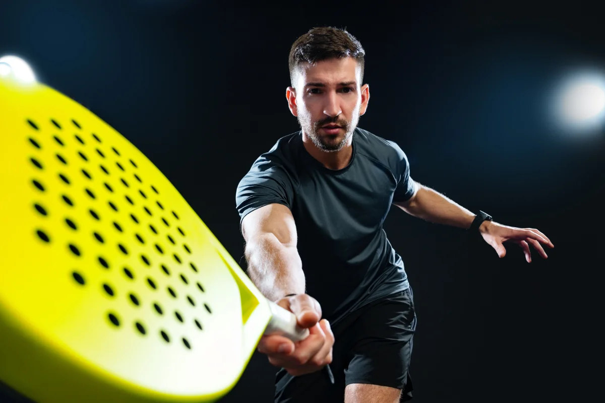 Man playing padel reaching forward to strike the ball with a yellow padel racket during an intense rally